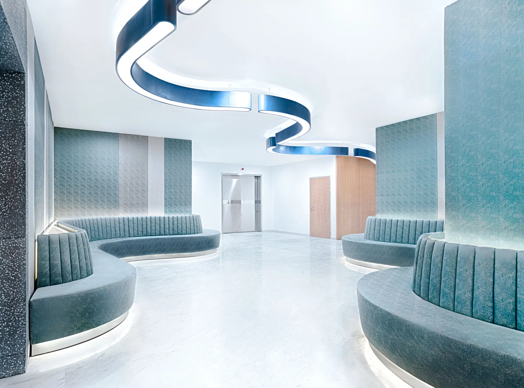Waiting area with curved teal banquettes under a winding blue ceiling light, Radiology, Shanghai International Medical Center