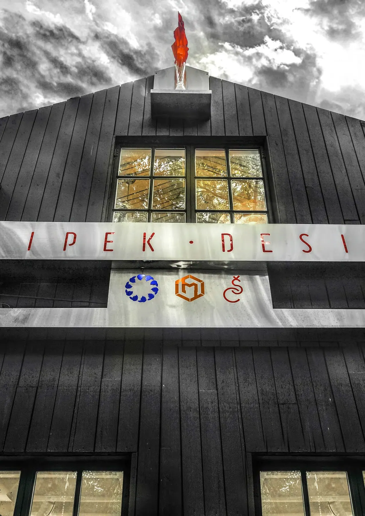Dark board-clad facade with shop sign and a red flame-shaped rooftop sculpture, Sipek Design shop, Shanghai